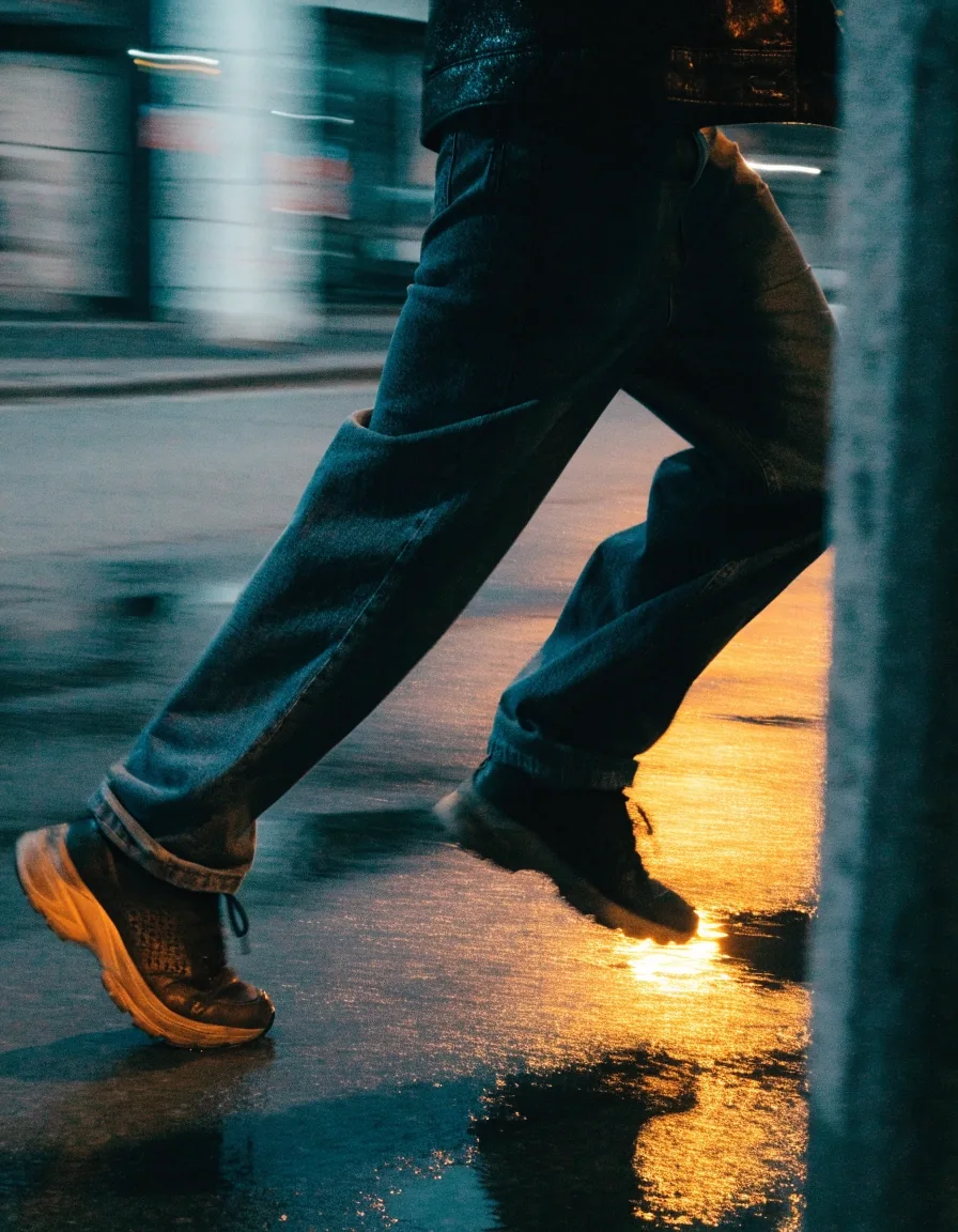 Worn sneakers on wet pavement under sodium streetlight, low angle